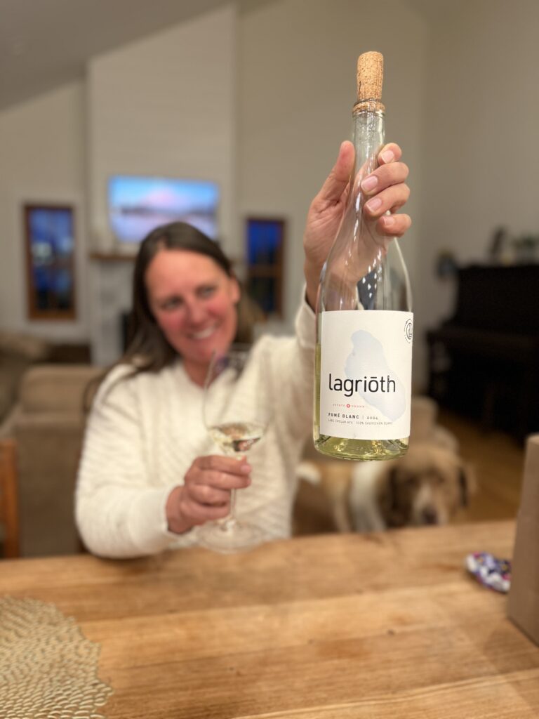 Jeana holding a bottle of Lagriōth Fumé Blanc at the table, raising a glass on a Saturday evening